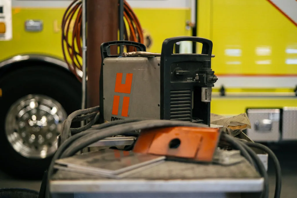 Plasma cutting power supply staged near a fire apparatus wheel in the FES shop